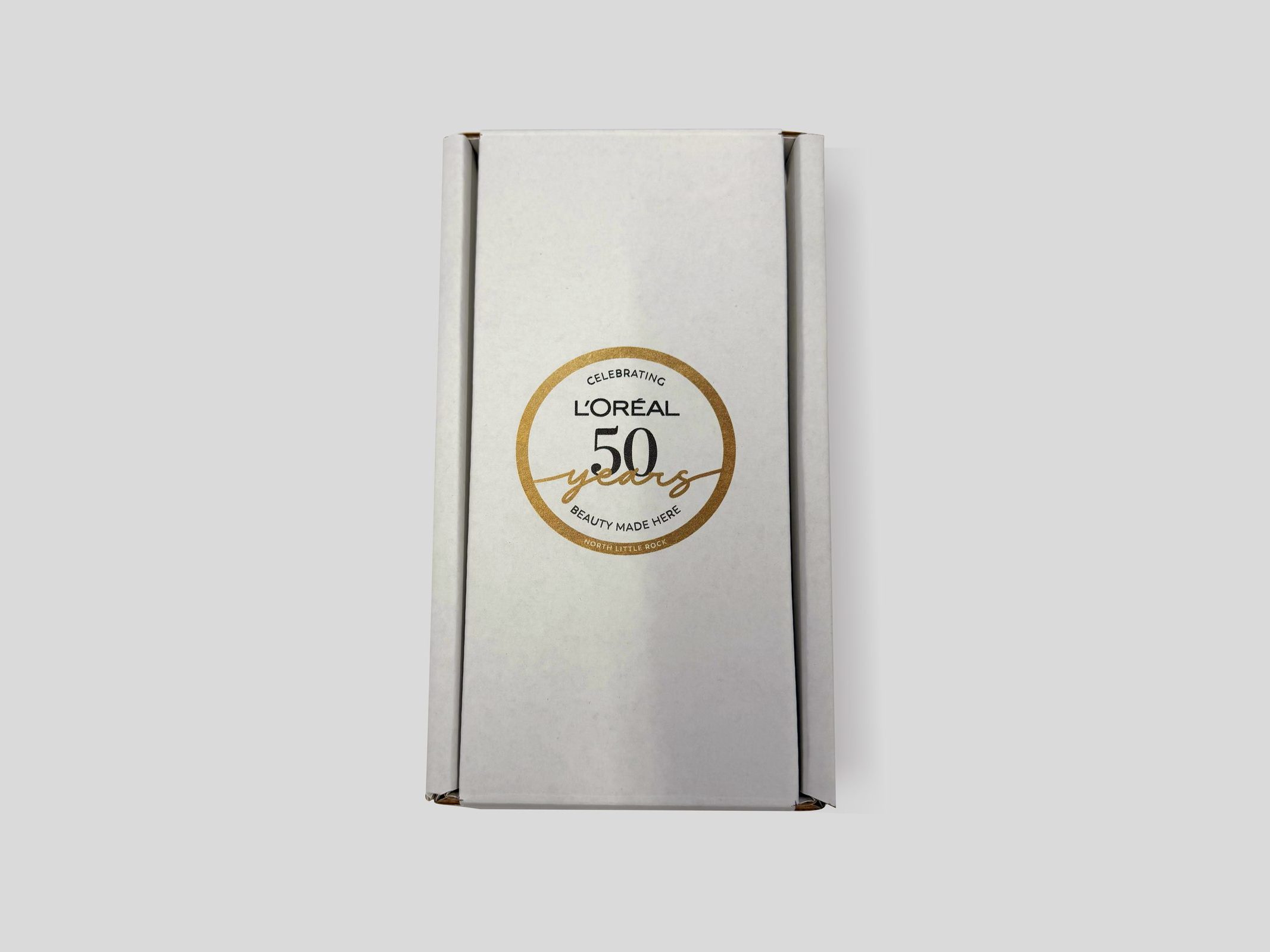 White L'Oréal 50th-anniversary mailer box with a gold seal, closed, by VSL Packaging
